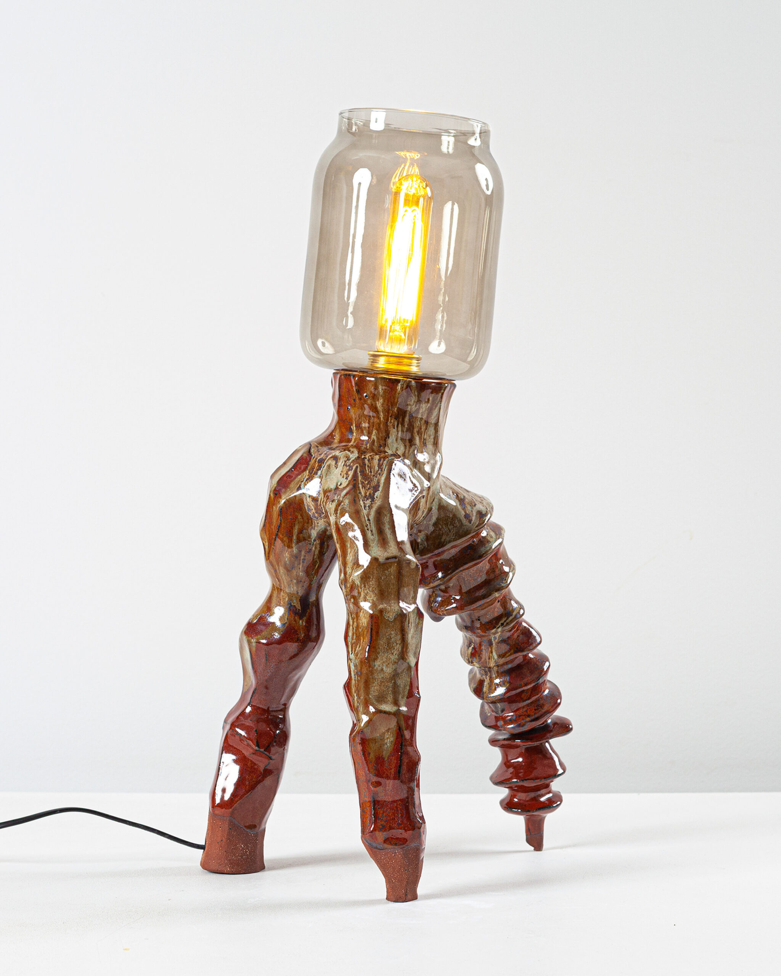 Glazed ceramic tripod lamp by Pia Isaia, with a smoked-glass shade over a lit filament bulb.